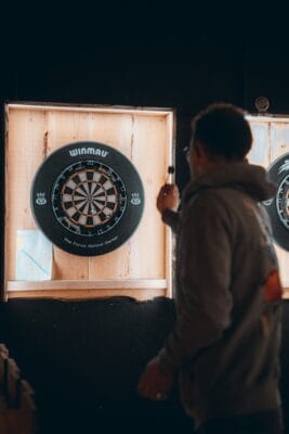 Dartspieler mit Dartpfeil vor einer beleuchteten Dartscheibe