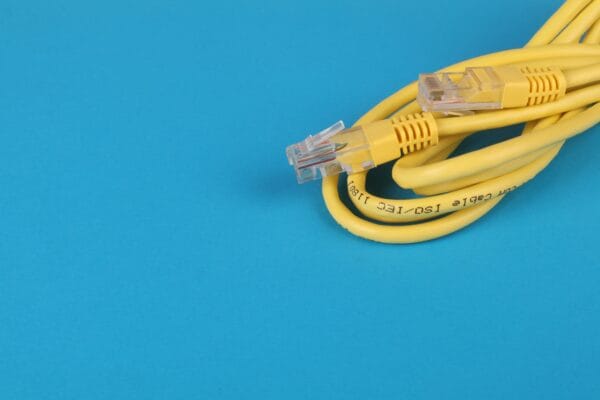 Aufgerolltes gelbes Ethernet-Netzwerkkabel mit zwei transparenten RJ45-Steckern auf blauem Hintergrund