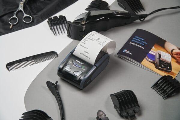 Mobiler Thermodrucker mit Kassenbon zwischen Friseurzubehör wie Haarschneider, Kamm und Schere