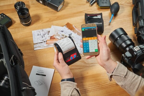 Mobiler Thermodrucker mit Kassenbon neben einem Smartphone mit geöffneter Kassen-App