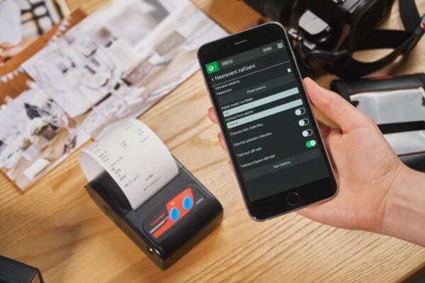 Smartphone mit Druckereinstellungen neben einem mobilen Thermodrucker mit Kassenbon