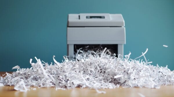 Großer Haufen zerkleinerten Papiers auf einer Holzfläche vor einem hellgrauen Aktenvernichter.