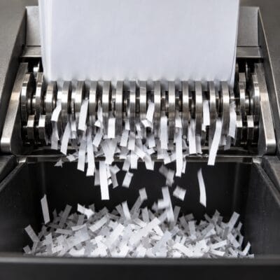 Metallisches Schneidwerk eines Aktenvernichters zieht weißes Papier ein und zerkleinert es.