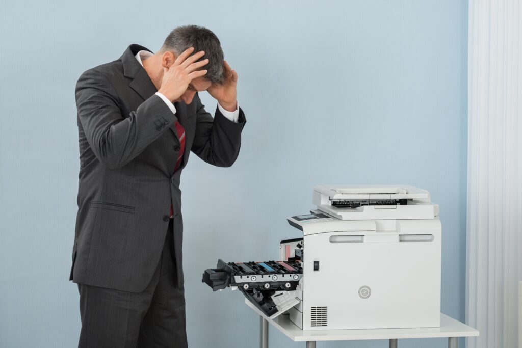 Mann hält sich neben einem geöffneten Bürodrucker mit beiden Händen den Kopf.
