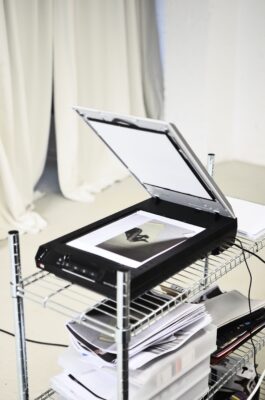 Schwarzer Flachbettscanner mit geöffnetem Deckel und einer Bildvorlage auf der Glasfläche.