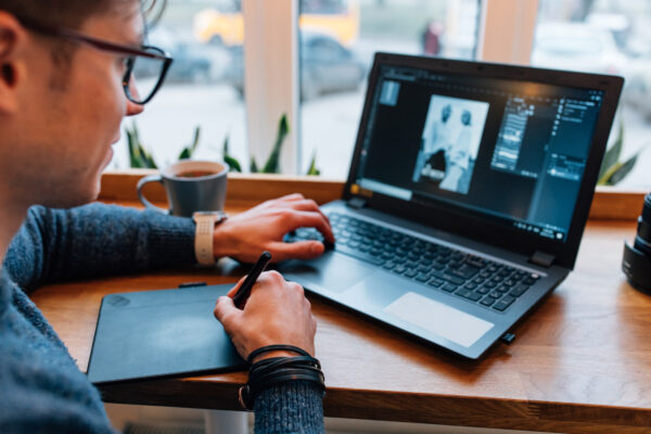 Ein Mann bearbeitet ein Foto am Laptop und verwendet dabei einen Eingabestift auf einem angeschlossenen Grafiktablett.