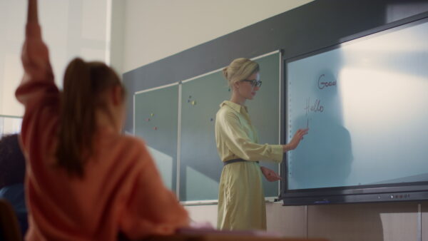 Lehrerin erklärt vier Kindern ein Dreieck und markiert mit einem Stift einen Winkel auf einem interaktiven Whiteboard.