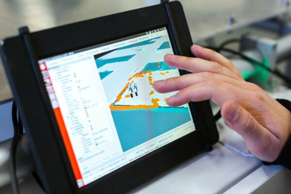 Hand bedient ein Tablet mit schwarzem Schutzrahmen und einer technischen Karte mit orangefarbenen und türkisfarbenen Markierungen.