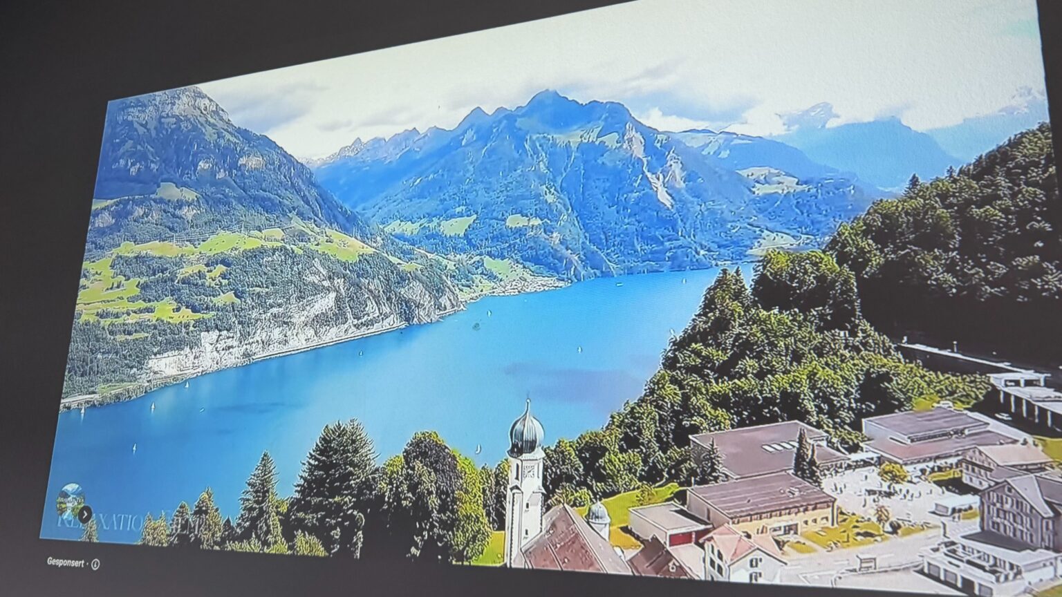 Vom Tablet übertragenes YouTube-Video mit einer See- und Berglandschaft auf der Projektionsfläche.